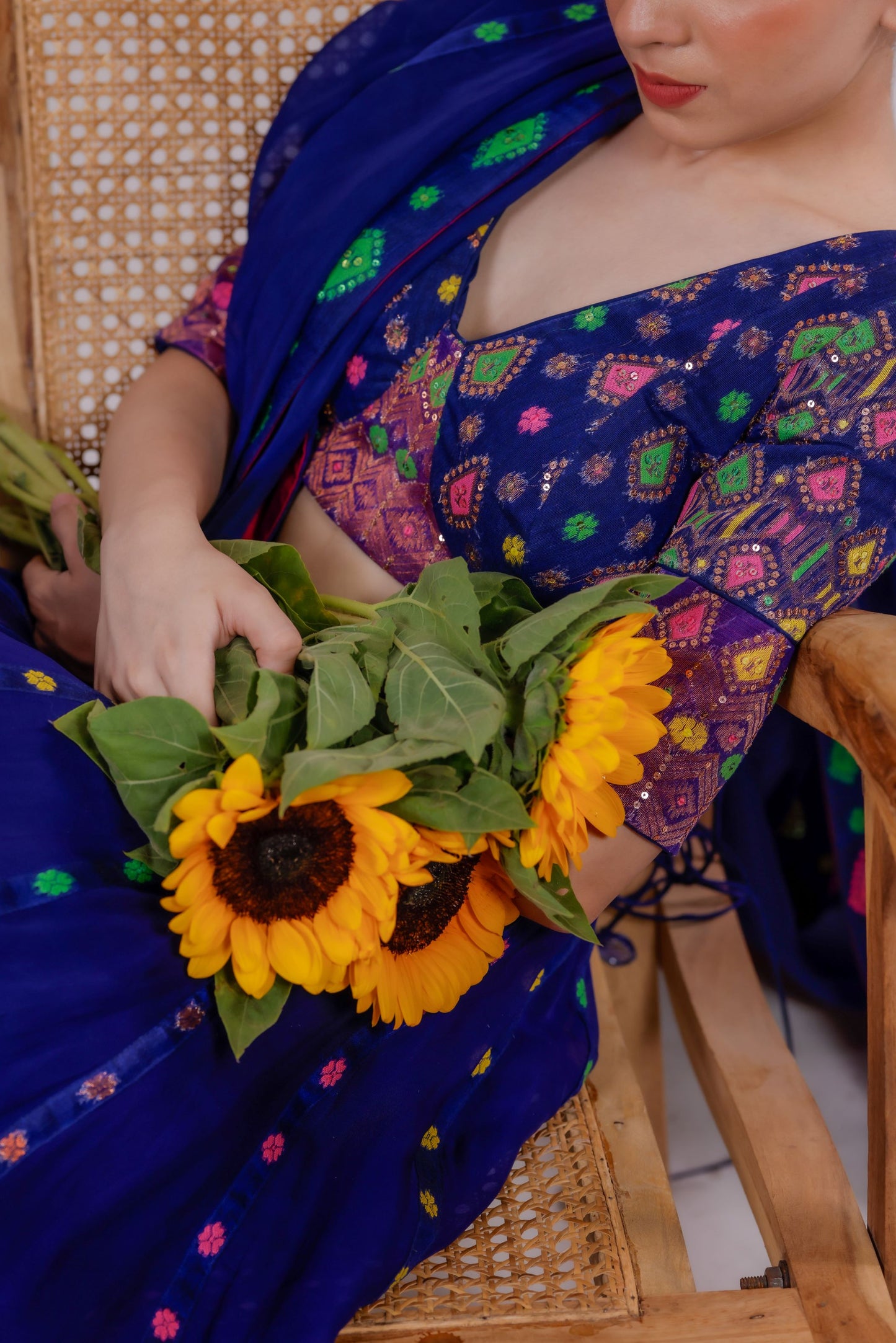 Person wearing a colorful traditional outfit holding sunflowers.